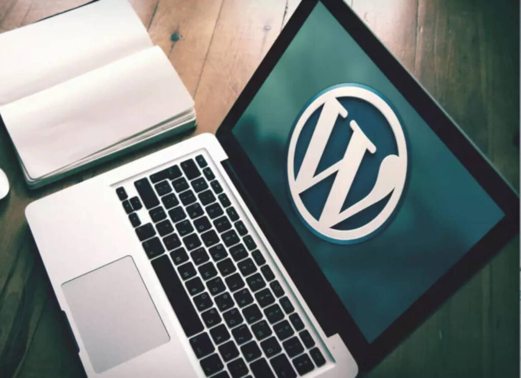Macbook next to a notebook and WordPress' logo on the screen