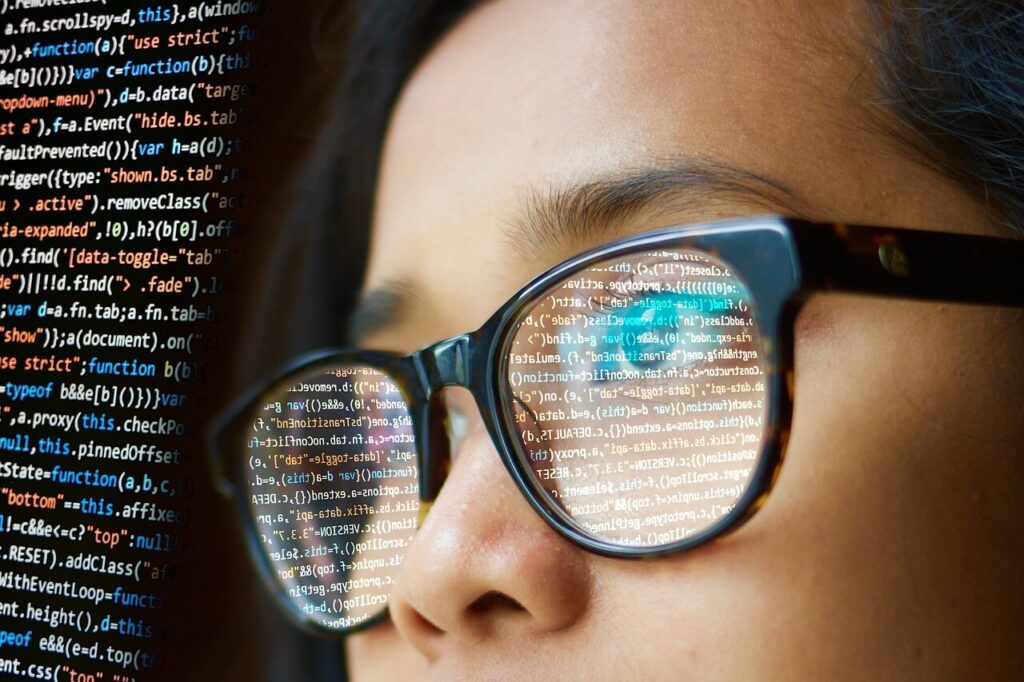woman with glasses looking at code on a screen