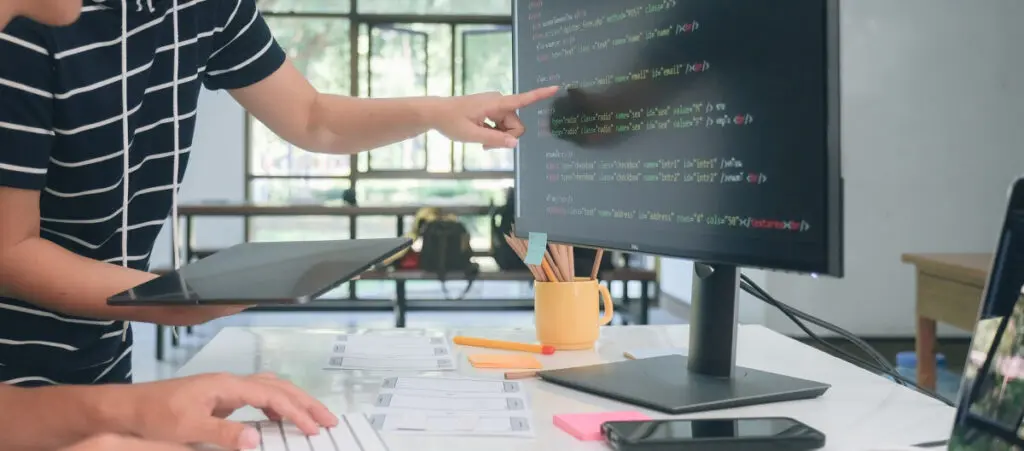 two WordPress developers examine HTML code on a large screen