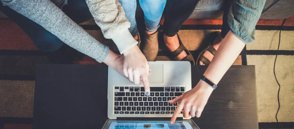 overhead view of a team of WordPress developers sitting on the same couch, all pointing to the screen of a single computer