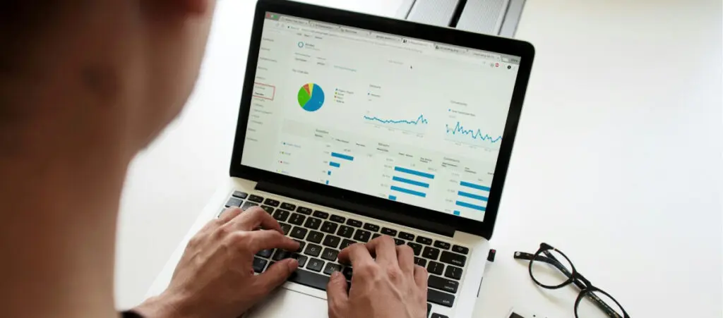 an over-the-shoulder closeup of someone using a laptop. The screen displays various graphs and statistics