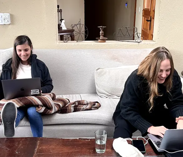 two WordPress agency team members sitting on a white couch, each using their laptops while working on a development project