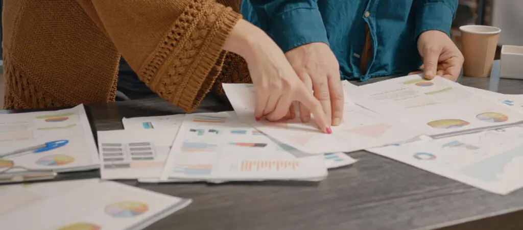 closeup of two people pointing at various papers on a table when assigning billable hours to a project