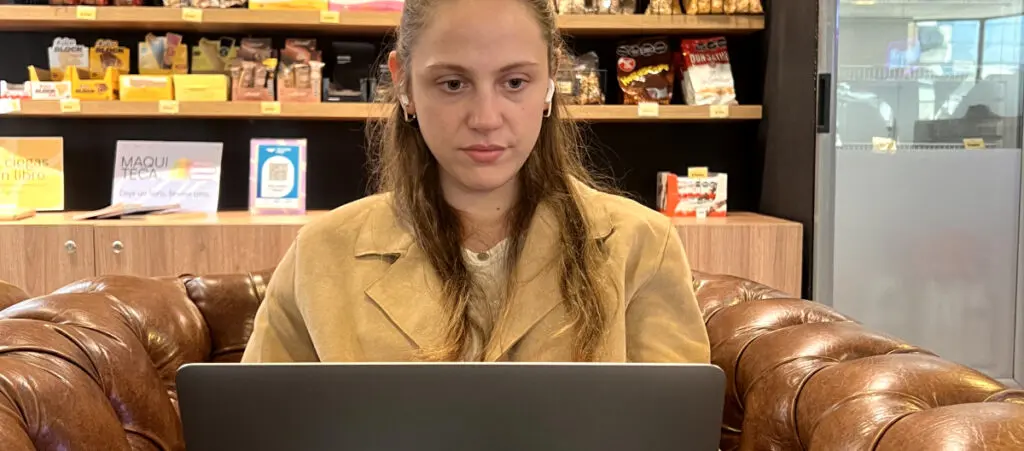 A WordPress project manager sitting on a couch with her laptop on her lap while wearing wireless earphones