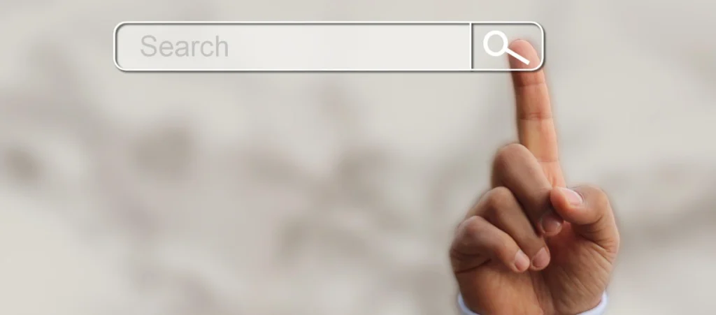 a search engine bar, with a hand comning into frame to place its index finger directly in the "Search" button