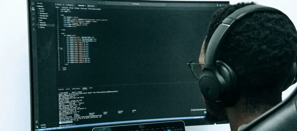 man writing programming code while wearing headphones