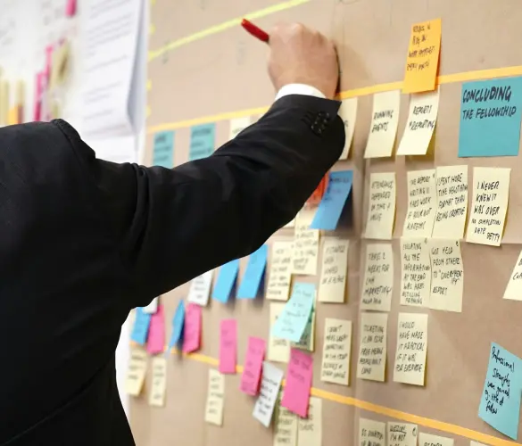 man writing on a post-it note that is surrounded by more post-it notes on a board