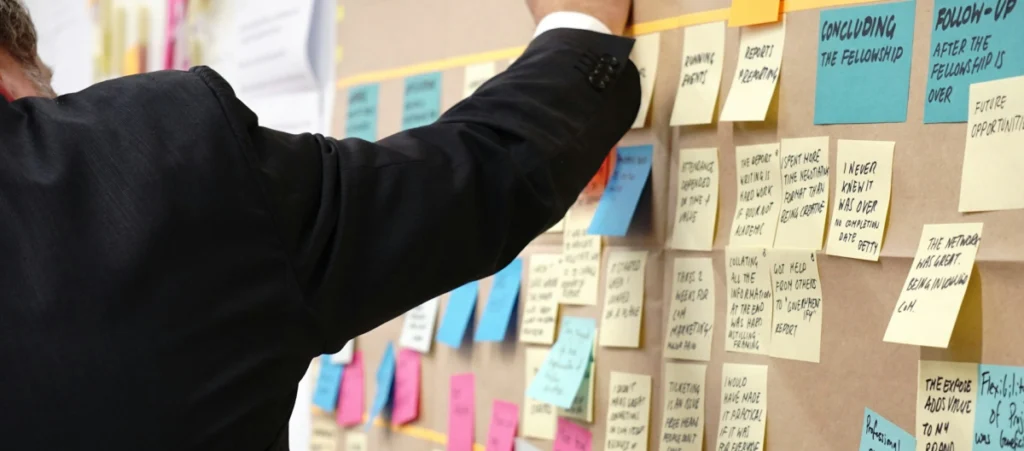 man writing on a post-it note that is surrounded by more post-it notes on a board